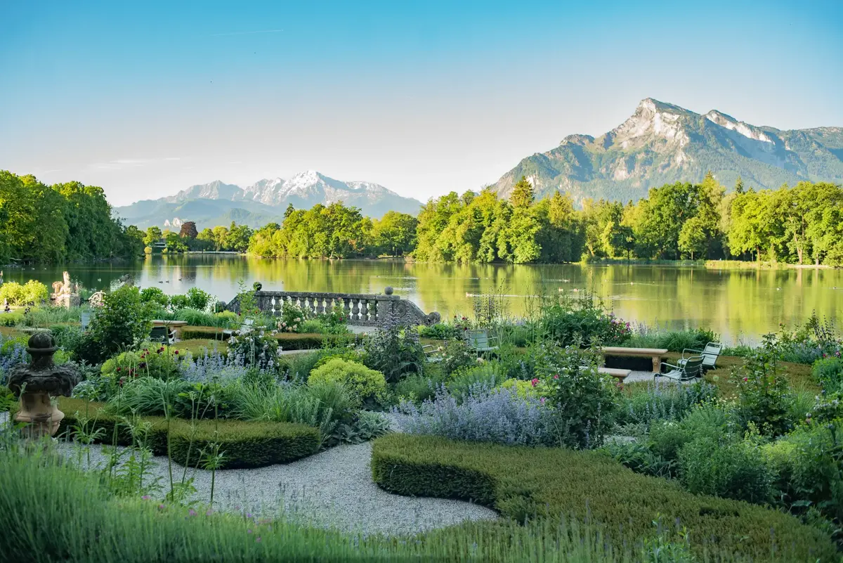 Blick vom Rosengarten des Schlossgarten Leopoldskron über den Schlossteich auf die Salzburger Alpen bei Sonnenaufgang.