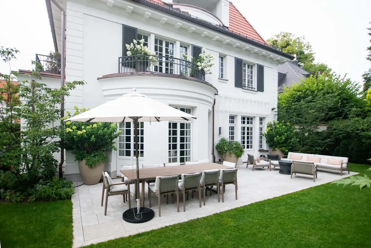 Großzügige Terrasse mit langer Tafel, Lounge-Sitzgruppe und Sonnenschirm vor der klassischen Stadtvilla im Villengarten München-Bogenhausen.