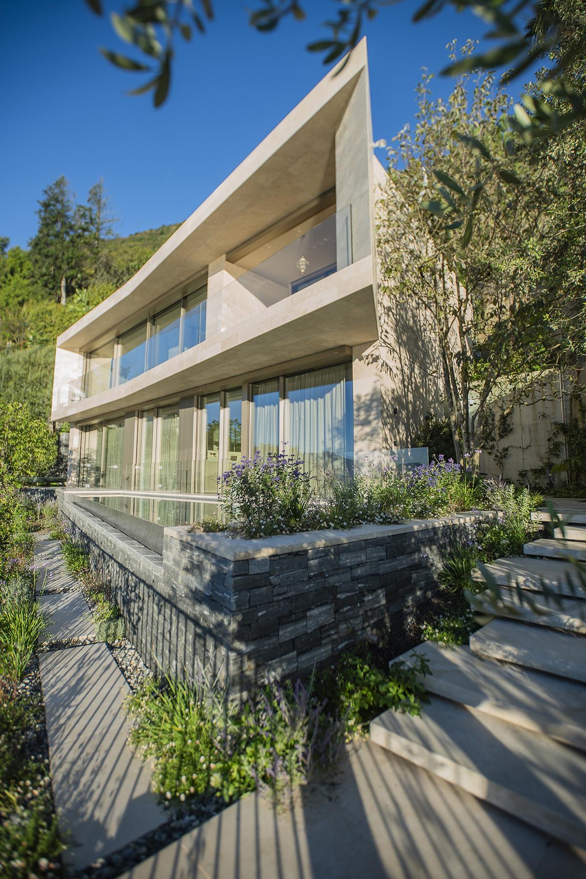 Moderne Villa mit klarer Architektur, Natursteinmauer und mediterranem Pflanzkonzept.